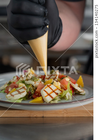 The chef seasons the salad with sauce. The chef seasons the salad with sauce. 134140275