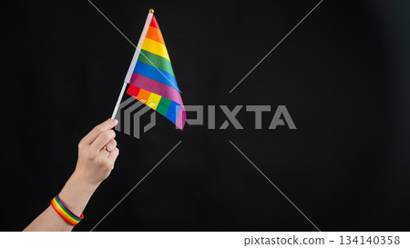 Woman with wedding ring holding rainbow flag on black background.  134140358
