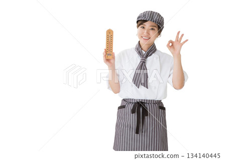 A woman wearing a chef's coat holding a thermometer A woman wearing a chef's coat holding a thermometer 134140445