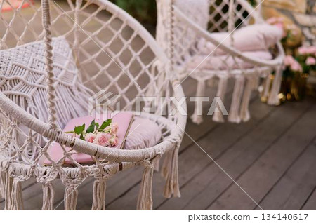 The swing is light wicker with a soft pillow in the style of macrome. Boho style, garden design. The swing is light wicker with a soft pillow in the style of macrome. Boho style, garden design. 134140617