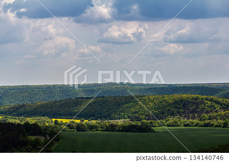 Lush green landscape under a cloudy sky with rolling hills valleys and vibrant foliage 134140746
