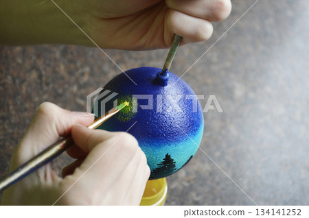 Female hands carefully painting a Christmas ball in vibrant blue hues Female hands carefully painting a Christmas ball in vibrant blue hues 134141252