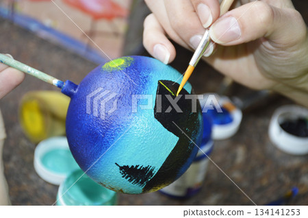 Female hands carefully painting a Christmas ball in vibrant blue hues 134141253