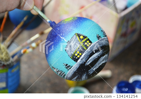 Female hands carefully painting a Christmas ball in vibrant blue hues Female hands carefully painting a Christmas ball in vibrant blue hues 134141254