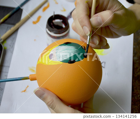Female hands carefully painting a Christmas ball in vibrant orange hues Female hands carefully painting a Christmas ball in vibrant orange hues 134141256