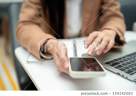 Close up businesswoman office worker's hand holding phone over laptop and notebook on table in cafe. Close up businesswoman office worker's hand holding phone over laptop and notebook on table in cafe. 134142083