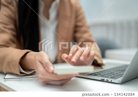 Close up businesswoman office worker's hand holding phone aside laptop and notebook on table in cafe Close up businesswoman office worker's hand holding phone aside laptop and notebook on table in cafe 134142084