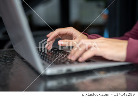 Close up of a man student's hand typing on laptop's keyboard on shiny black table in cafe or library Close up of a man student's hand typing on laptop's keyboard on shiny black table in cafe or library 134142299