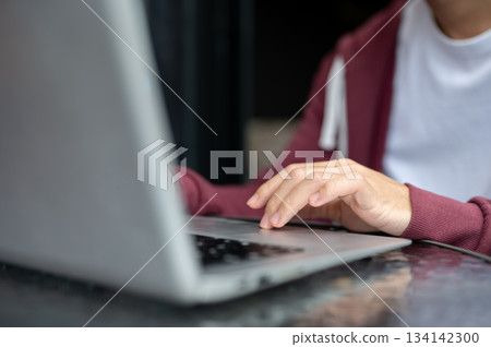 Close up of a man student's hand typing or tapping on laptop at shiny black table in cafe or library Close up of a man student's hand typing or tapping on laptop at shiny black table in cafe or library 134142300