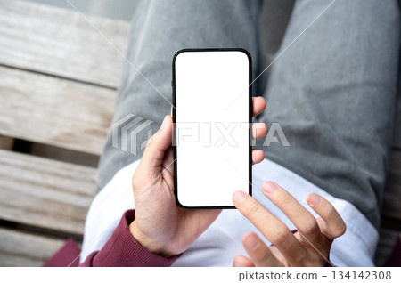 A man's hands holding blank screen smartphone with fingers hovering sitting outdoor on wooden bench. A man's hands holding blank screen smartphone with fingers hovering sitting outdoor on wooden bench. 134142308