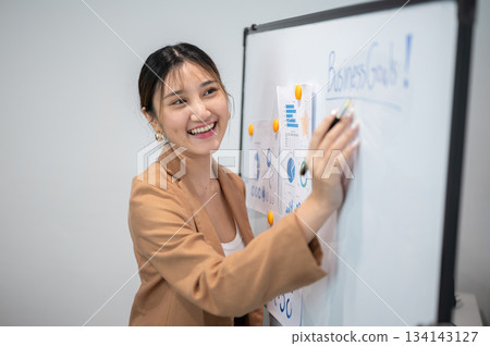 Asian businesswoman office worker holding a pen under chain looking at laptop on table in white room 134143127