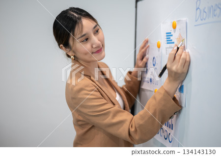 Asian businesswoman office worker holding a pen under chain looking at laptop on table in white room Asian businesswoman office worker holding a pen under chain looking at laptop on table in white room 134143130