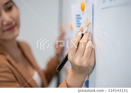 Asian businesswoman office worker holding a pen under chain looking at laptop on table in white room 134143131
