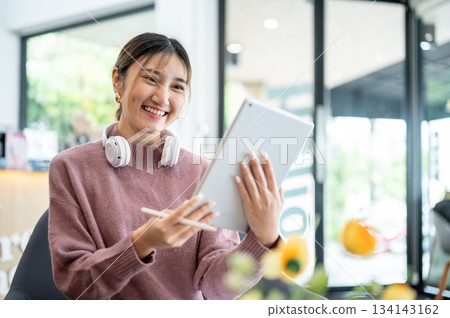 Asian businesswoman office worker holding a pen under chain looking at laptop on table in white room 134143162