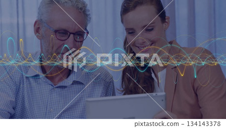 Senior man and colleague analyzing tablet data at table in office, with waveforms and eyeglasses Senior man and colleague analyzing tablet data at table in office, with waveforms and eyeglasses 134143378