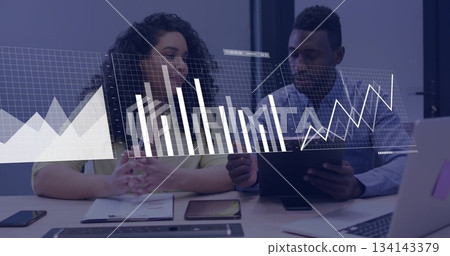 Analysts analyzing data overlay in business attire at office conference desk with laptop and tablet Analysts analyzing data overlay in business attire at office conference desk with laptop and tablet 134143379