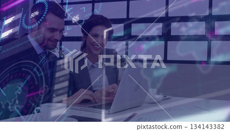 Smiling colleagues in business attire reviewing chart overlay on laptop at office, with coffee cup 134143382