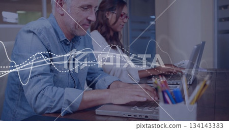 Typing man wearing denim shirt on laptop in office, with pencil holder and waveforms, copy space 134143383