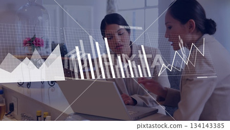 Analyzing data women wearing blazers gesturing toward laptop at office counter, with digital graphs Analyzing data women wearing blazers gesturing toward laptop at office counter, with digital graphs 134143385