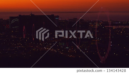 Showing skyline with high-rise buildings glowing at dusk from hillside ridge, with lens flares 134143428