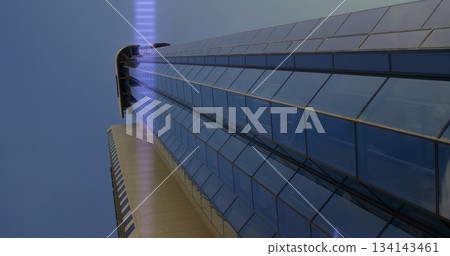 Shining glass skyscraper rising at street-level city view, with concrete base and purple LED strip 134143461