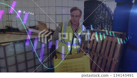 Worker wearing safety vest, gloves and goggles lifting yellow crate in warehouse, with AR overlays 134143491