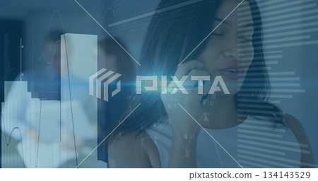 Talking on smartphone, woman in sleeveless top at office, with monitors, chart overlays, copy space 134143529