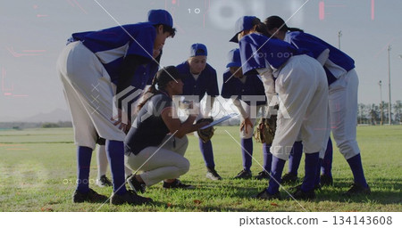 Huddling softball team listening to coach kneeling with clipboard in outfield, blue jerseys, gloves Huddling softball team listening to coach kneeling with clipboard in outfield, blue jerseys, gloves 134143608