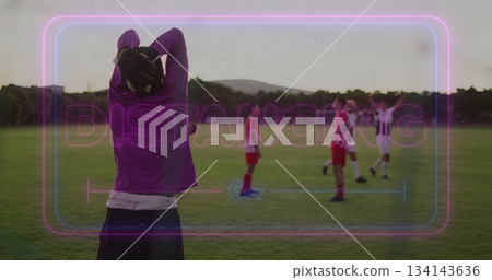 Standing spectator in purple hoodie monitoring players on pitch with distancing overlay, copy space 134143636