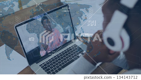 Watching coworker holding tablet and gesturing on laptop screen at home office desk with headphones Watching coworker holding tablet and gesturing on laptop screen at home office desk with headphones 134143712