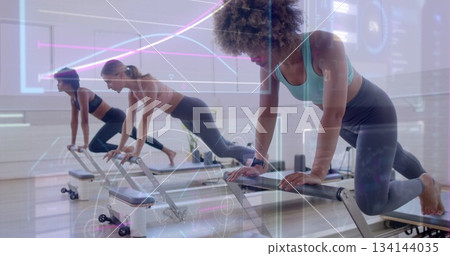 Three women holding high plank on reformer machines in fitness studio, with resistance straps Three women holding high plank on reformer machines in fitness studio, with resistance straps 134144035