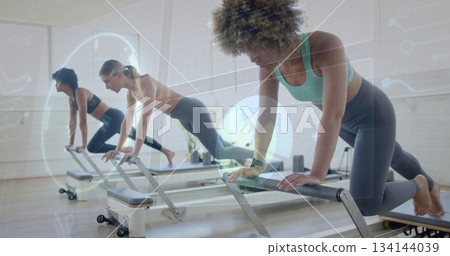Exercising three women in sports bras, leggings on Pilates reformers in studio, with HUD overlay Exercising three women in sports bras, leggings on Pilates reformers in studio, with HUD overlay 134144039