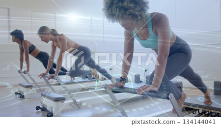 Three women performing reformer plank in Pilates studio with reformer machines and resistance bands Three women performing reformer plank in Pilates studio with reformer machines and resistance bands 134144041