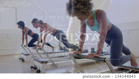 Three women wearing sportswear holding planks on Pilates reformers in studio with fitness watches Three women wearing sportswear holding planks on Pilates reformers in studio with fitness watches 134144043