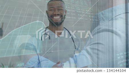 Doctor in scrubs with stethoscope shaking hands with patient in clinic, with projections over desk 134144104