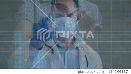 Male doctor examining blood sample vial in clinical lab, with gloves masks stethoscope and graphs 134144187