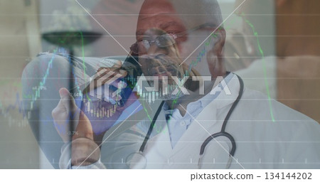 Speaking senior physician in white coat holding smartphone at clinic, stethoscope and market charts Speaking senior physician in white coat holding smartphone at clinic, stethoscope and market charts 134144202