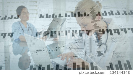 Typing doctor with stethoscope on laptop at clinic and nurse using tablet and graphs, copy space 134144348