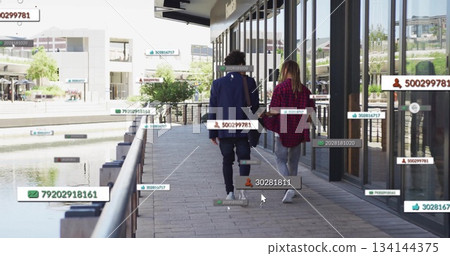 Walking couple holding hands along waterfront path under glass windows, with floating digital tags 134144375