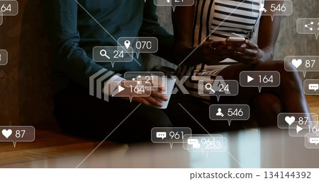 Sitting friends holding smartphone and coffee cup in cafe, floating social notification icons Sitting friends holding smartphone and coffee cup in cafe, floating social notification icons 134144392