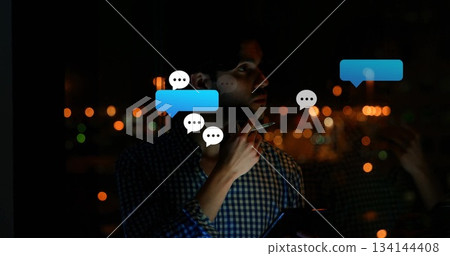 Standing man in checked shirt tapping stylus at chin holding tablet by office window, chat bubbles Standing man in checked shirt tapping stylus at chin holding tablet by office window, chat bubbles 134144408