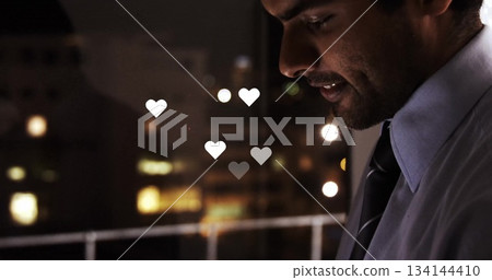 Standing employee wearing shirt and tie gazing at window in office, rising heart icons, copy space 134144410