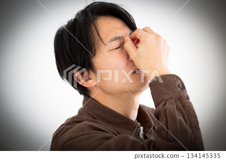 A middle-aged man suffering while holding the corners of his eyes 134145335