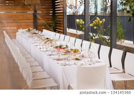Wide shot of long set table on terrace with city view - elegant table setting for event 134145360