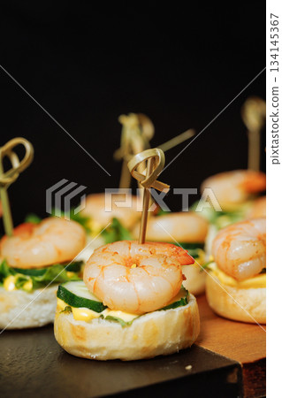 Close-up of canape with shrimp and cucumber on dark background - elegant appetizer 134145367