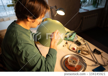 Man restorer working on renovation of old retro electric lamp, unscrewing lampshade with screwdriver Man restorer working on renovation of old retro electric lamp, unscrewing lampshade with screwdriver 134145921