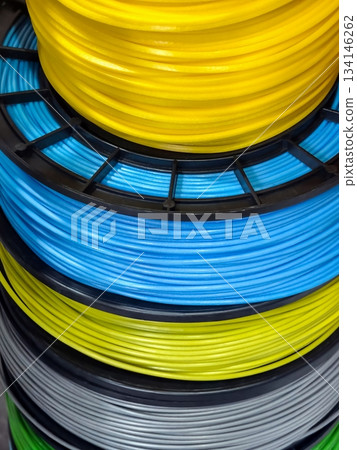 Different colors of plastic filament stacked in a workshop showing various spools of material for 3D printing use 134146262