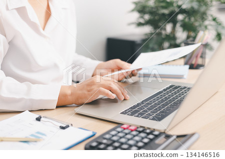 Businessperson typing on laptop with financial report and pen on office desk, concept of data analysis, digital business, accounting management, productivity and corporate finance planning. Businessperson typing on laptop with financial report and pen on office desk, concept of data analysis, digital business, accounting management, productivity and corporate finance planning. 134146516