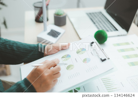 Eco-friendly business concept with hand analyzing financial charts and green earth globe symbolizing sustainable investment, environmental data analysis and green economy growth. green business. Eco-friendly business concept with hand analyzing financial charts and green earth globe symbolizing sustainable investment, environmental data analysis and green economy growth. green business. 134146624