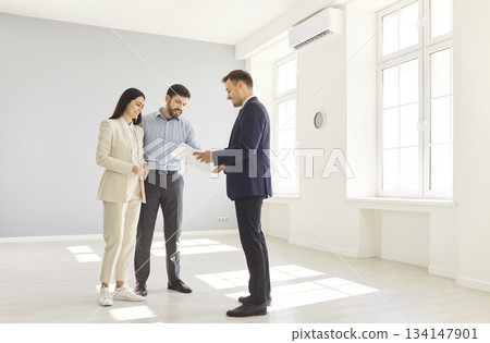 Young happy couple reaching agreement and going to sign a deal with a real estate agent. 134147901